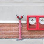 Outdoor fire hydrant and hoses against a brick wall, emphasizing fire safety.